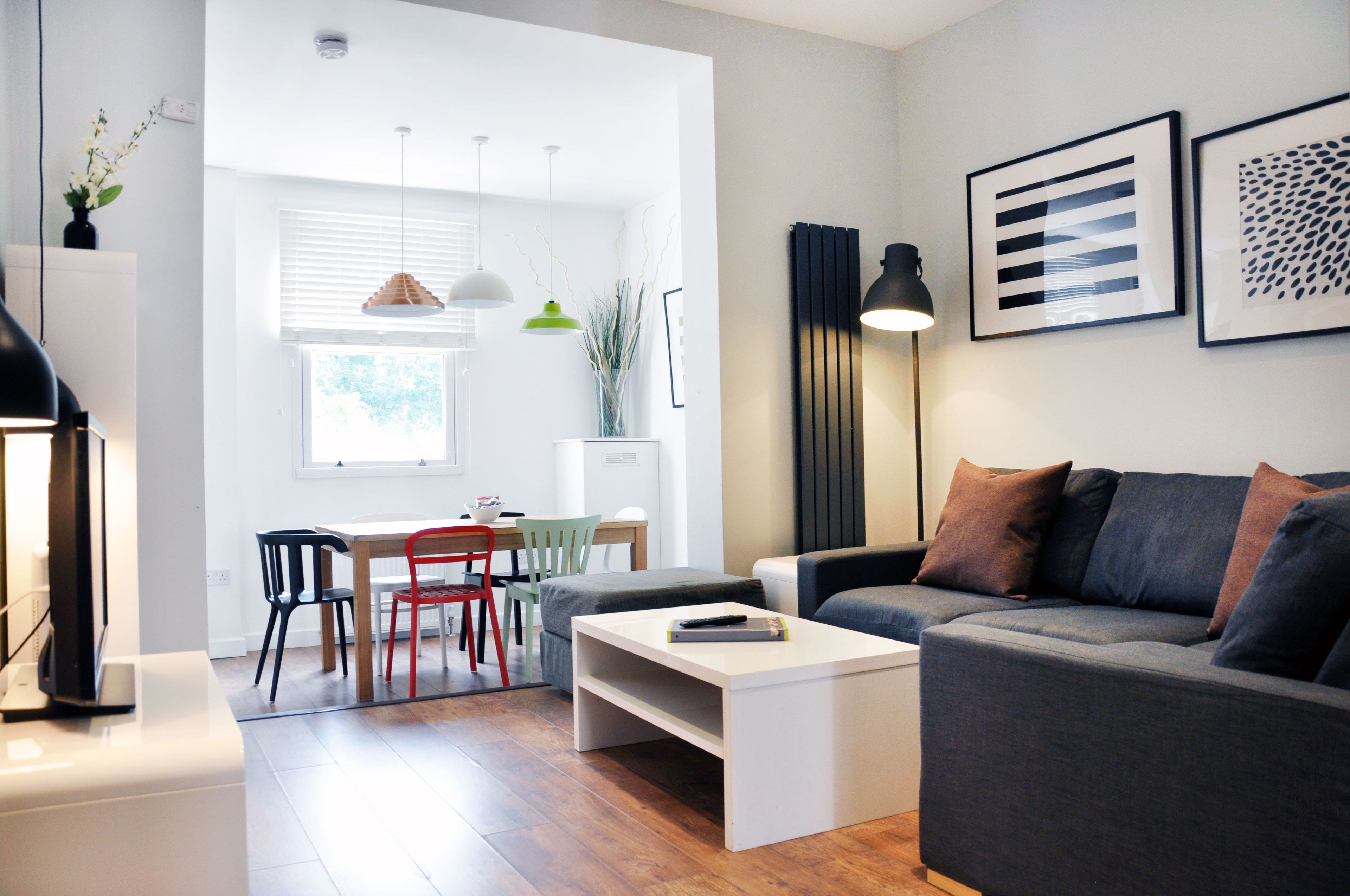 A modern living room with a grey sofa, a white coffee table, and a dining area with a table and chairs.