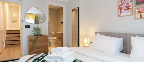 Une chambre d’hôtel avec un lit, une table de chevet avec une lampe, un miroir et un mur orné de tableaux.