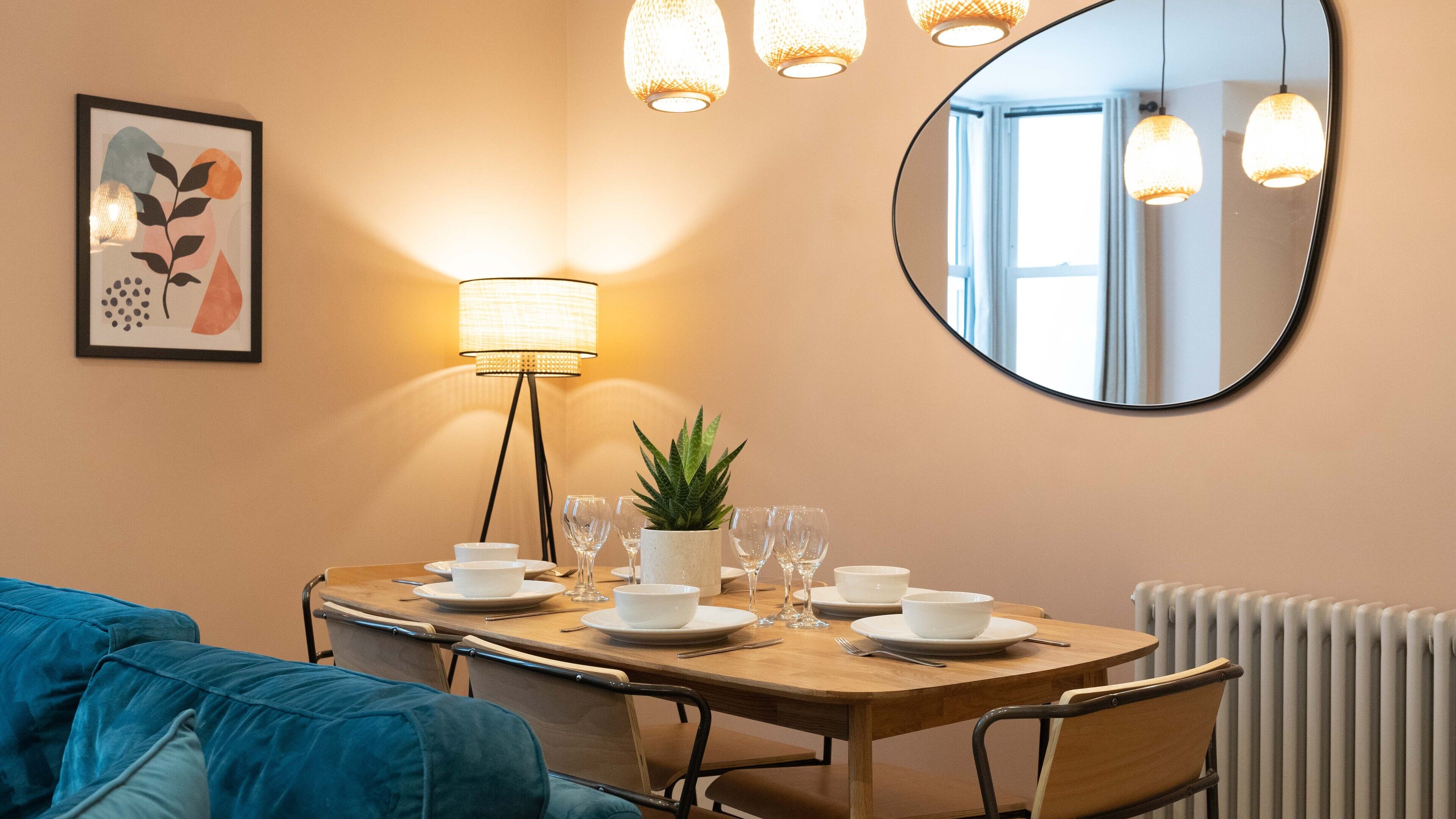 A dining area with a wooden table set for four, a potted plant, and a mirror on the wall.