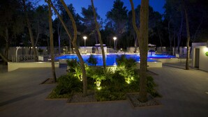 Zona de piscina nocturna con árboles circundantes y senderos iluminados.