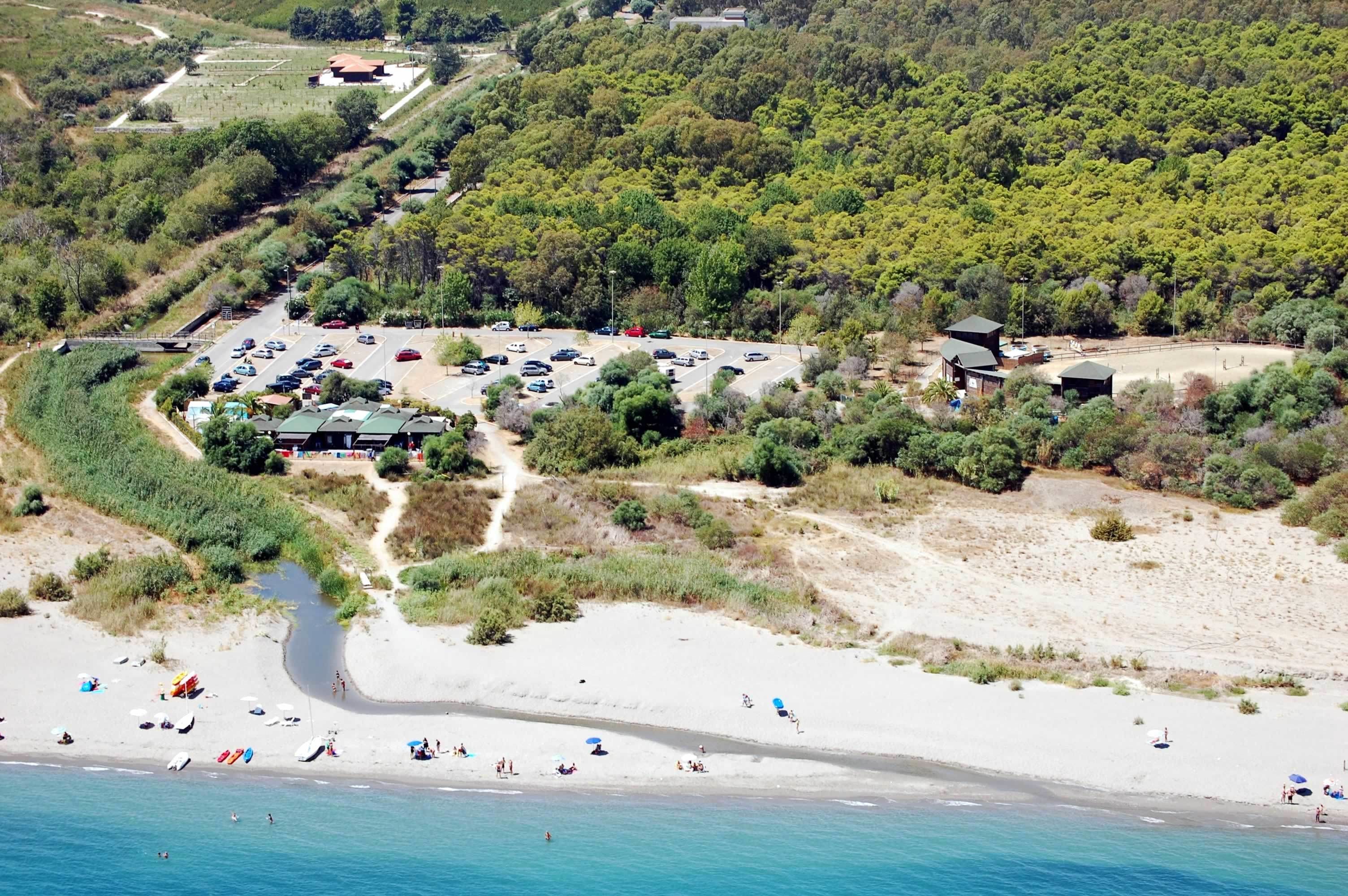 Luchtbeeld van een kustgebied met strand, parkeerplaats en gebouwen.