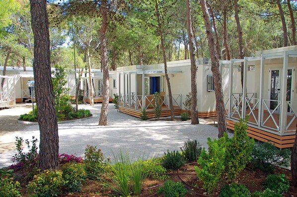 A row of mobile homes with outdoor decks, surrounded by trees and landscaped gardens.