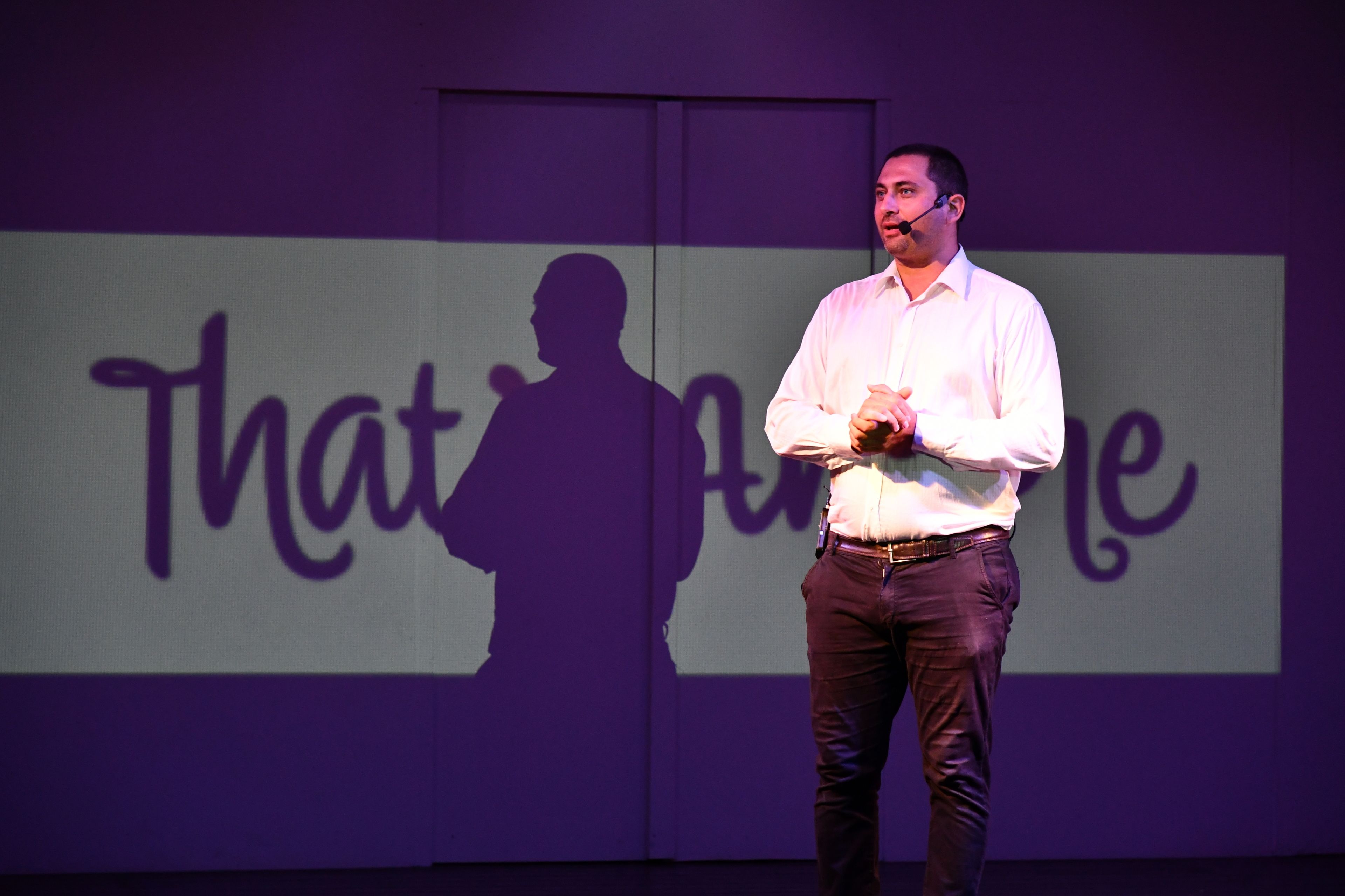 A person standing on a stage with a purple background and a silhouette of a person.