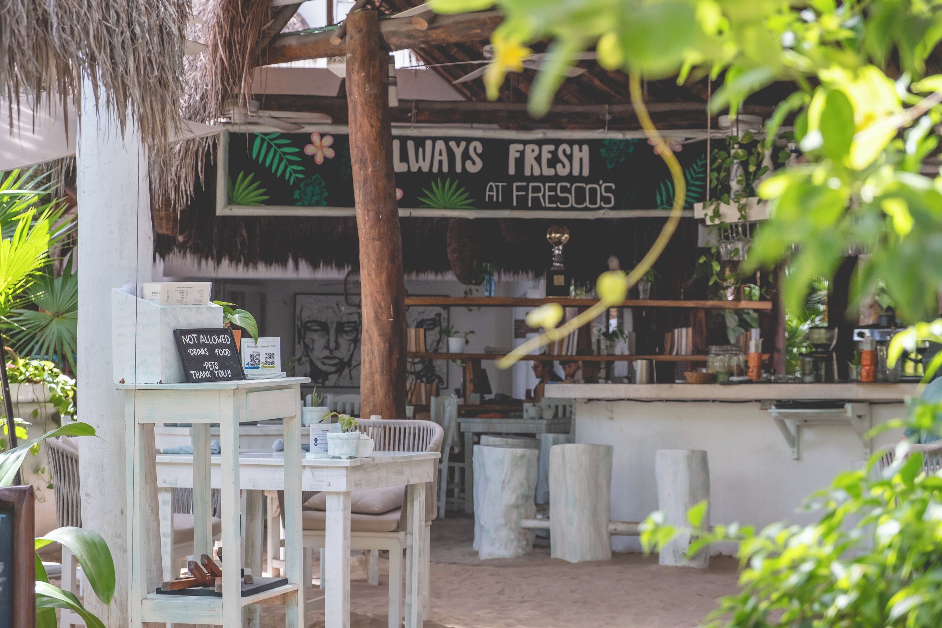 An outdoor seating area with a rustic aesthetic, featuring a sign that reads 'ALWAYS FRESH AT FRESCO'S' and a 'NOT ALLOWED DRINKS FOOD' sign.