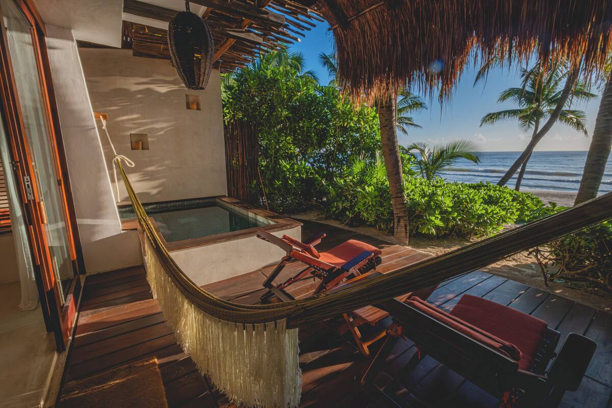 A hammock on a wooden deck with a view of the ocean and palm trees.