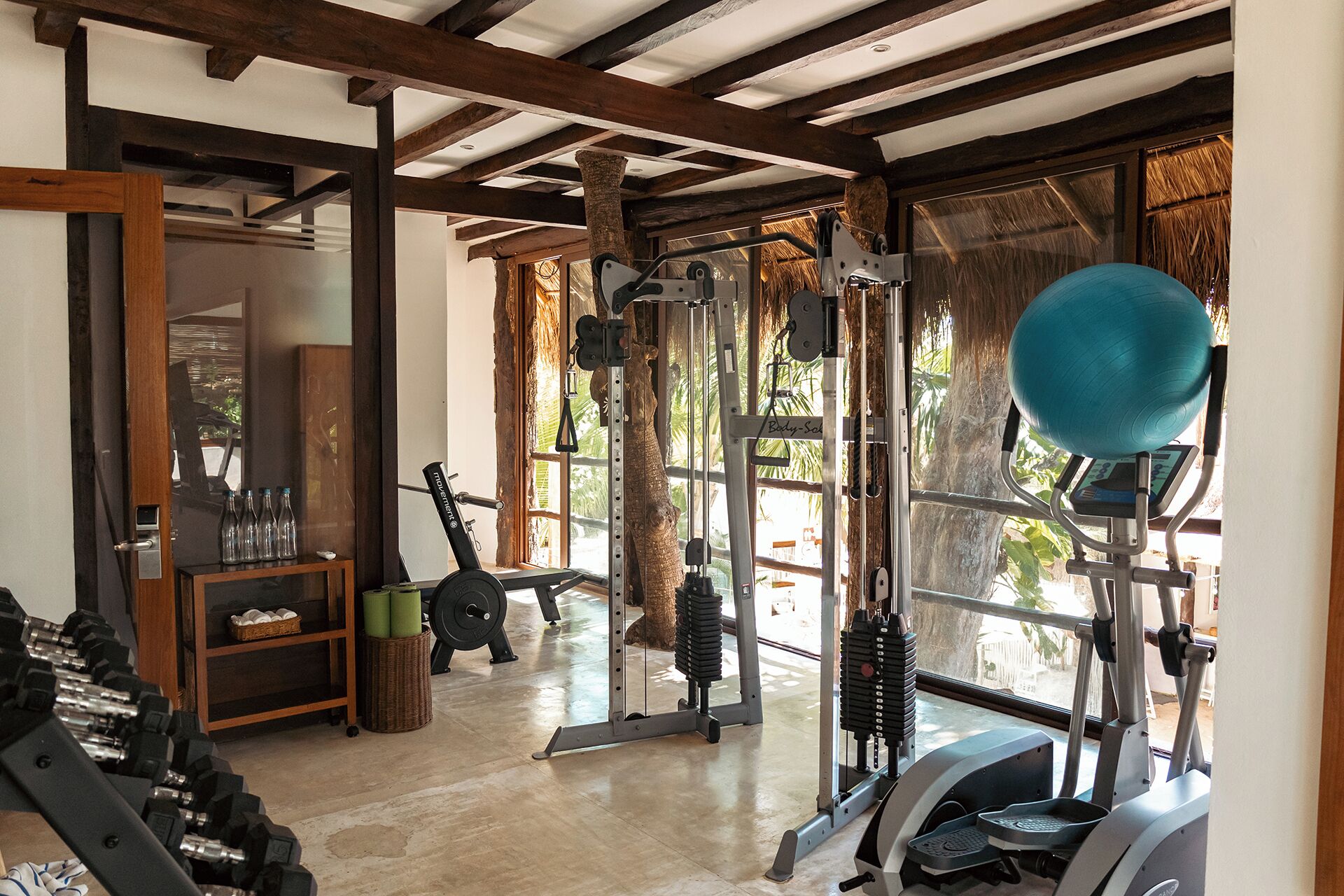 Une salle de sport équipée de divers appareils, notamment des haltères, un tapis de course et un vélo d’appartement.