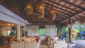 An indoor lounge area with a thatched roof, white sofas, and hanging wicker lamps. - The Beach Tulum Hotel (Tulum)