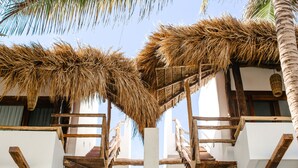 A building with a thatched roof, wooden balconies, and a staircase leading to an upper level. - The Beach Tulum Hotel (Tulum)