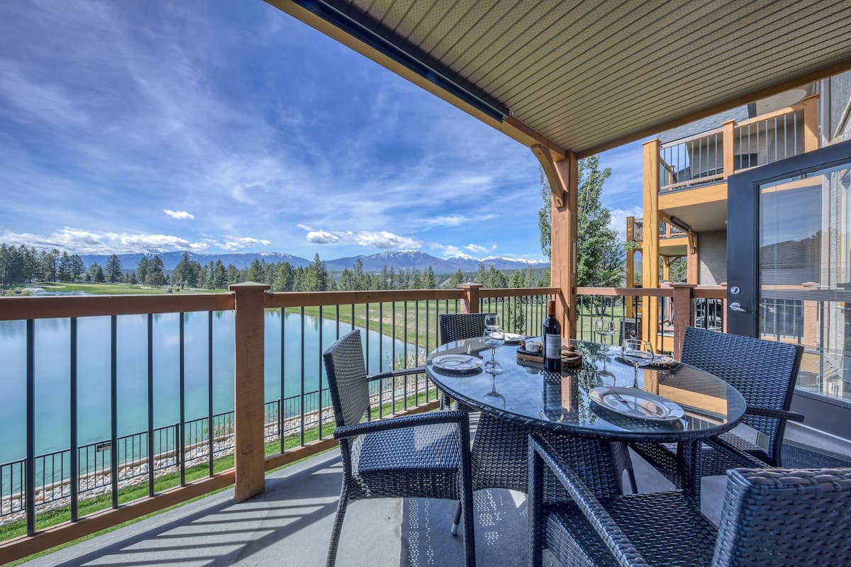 A balcony with a table set for dining, overlooking a lake and mountains.