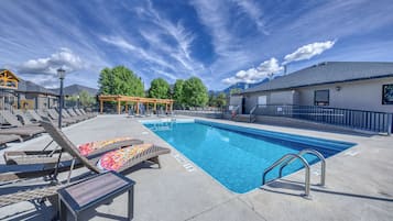 A swimming pool with lounge chairs and a pergola, surrounded by a fence and trees.