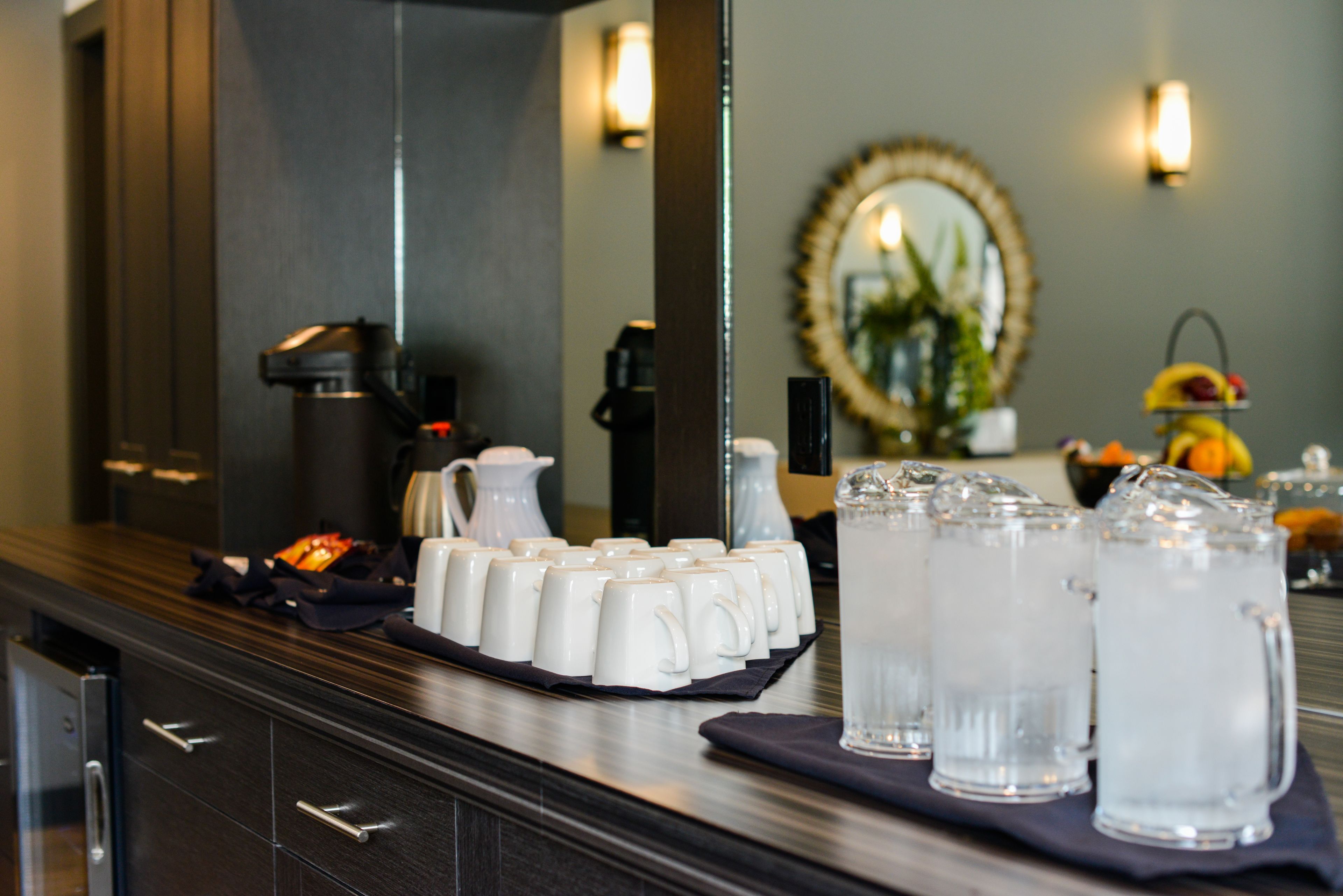 A hotel bar area with a tray of white mugs and several glasses of water.
