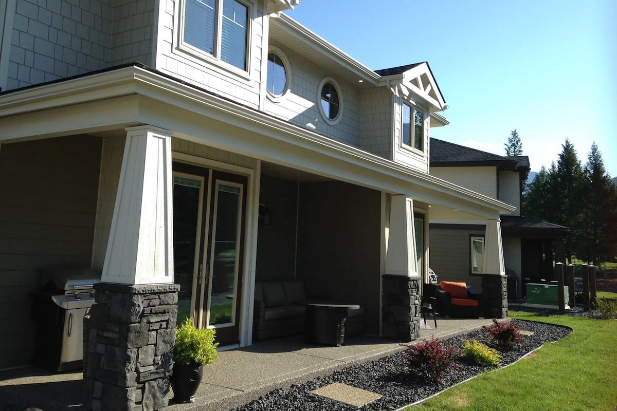 A two-story house with a covered patio, stone pillars, and a stone fireplace.