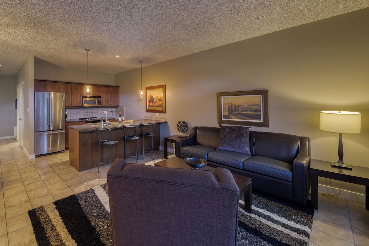 A modern kitchen with stainless steel appliances, a dining area with a sofa and a coffee table, and a living room with a couch and a lamp.
