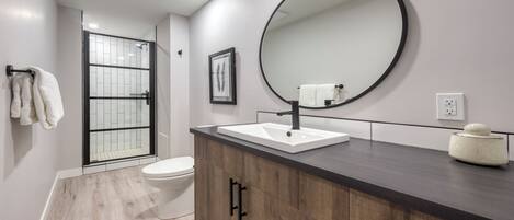 A modern bathroom with a large mirror, white sink, and wooden vanity.