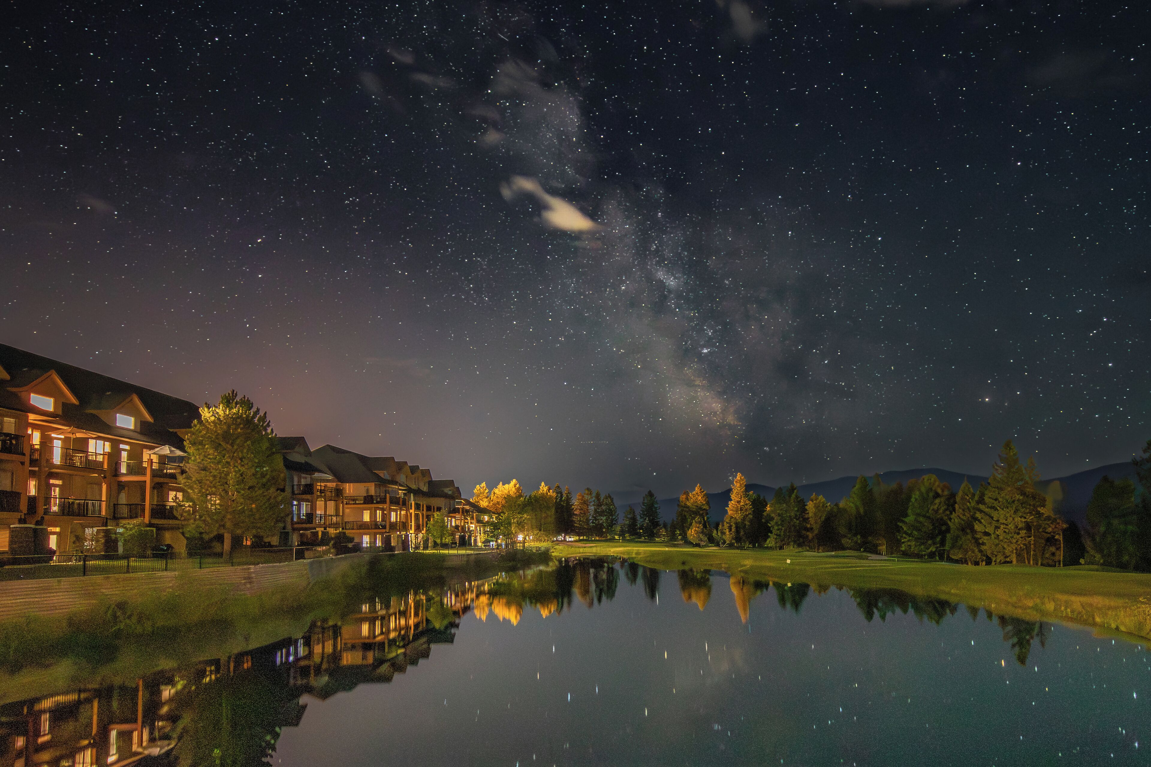 Una vista notturna di un hotel sul lago, con il riflesso degli edifici nell'acqua, cielo sereno e la Via Lattea ben visibile.
