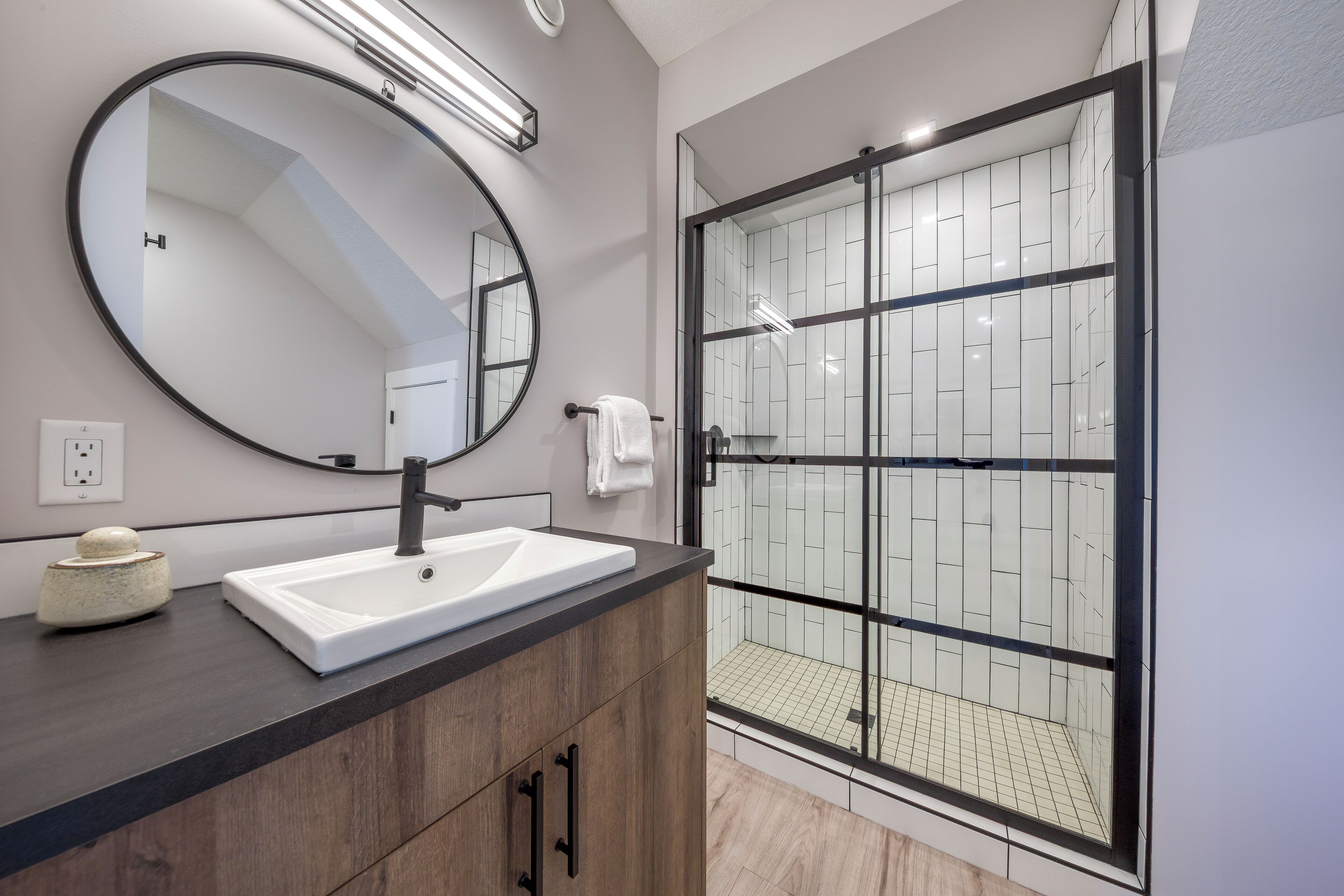 Une salle de bain moderne avec un grand miroir, un lavabo blanc et une douche à parois de verre.