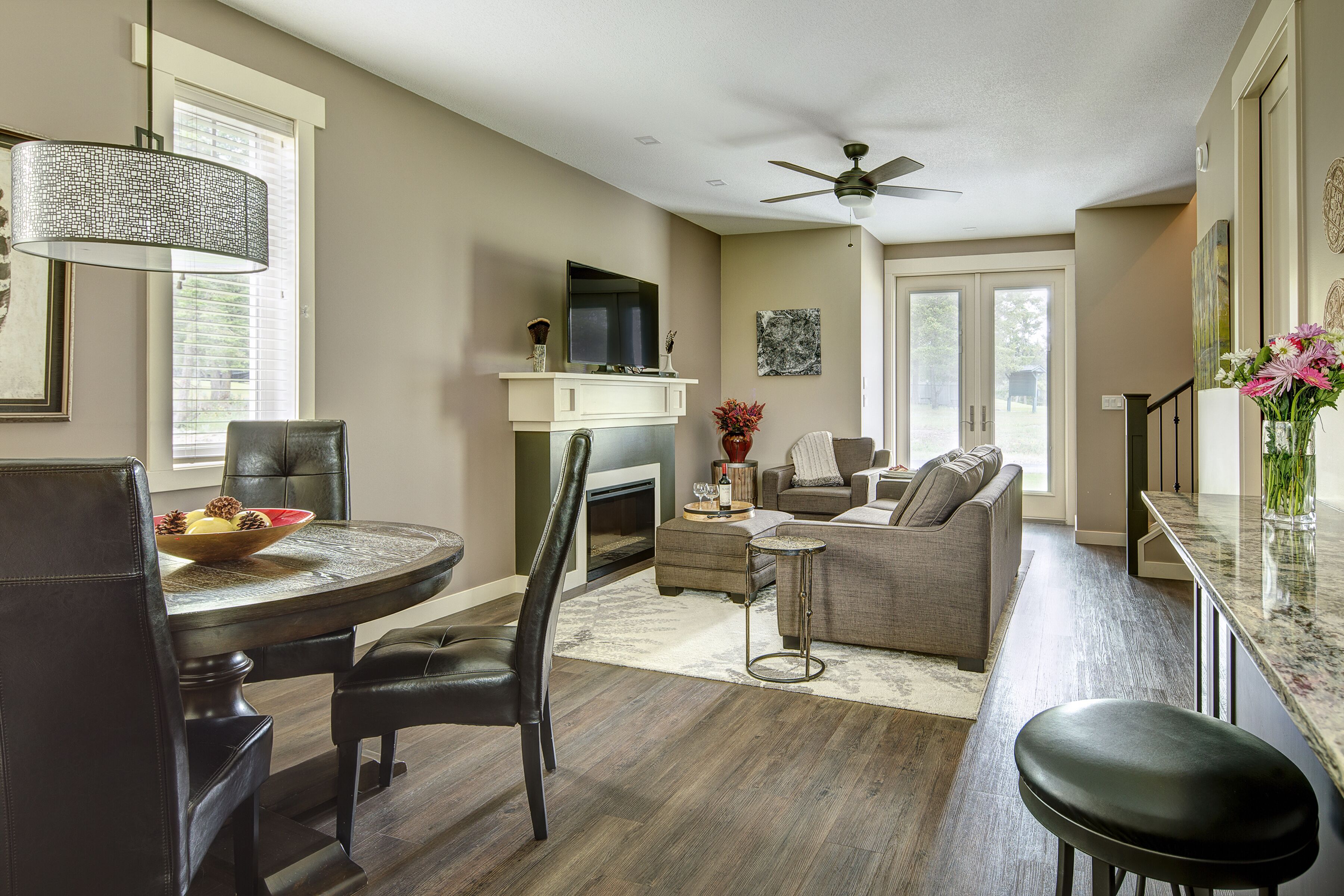 A modern living room with a fireplace, a dining area with a round table, and a kitchen with a bar.