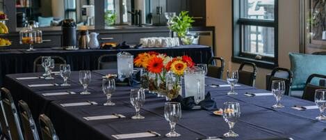 A long dining table set with chairs, a vase with flowers, and a pitcher of water.