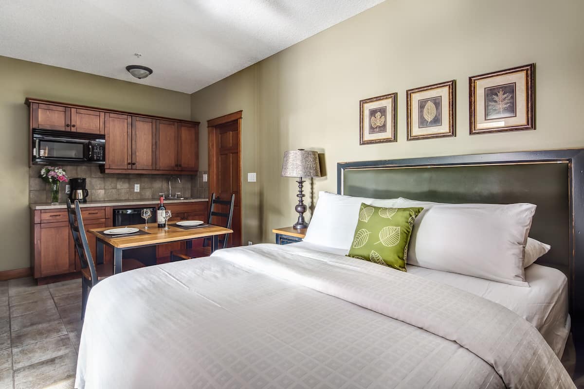 A hotel room with a bed, a dining table, a microwave, and a lamp.