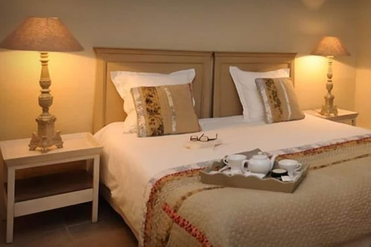 A neatly made bed with a tray of tea and cups, two bedside lamps, and a chair with a cushion.