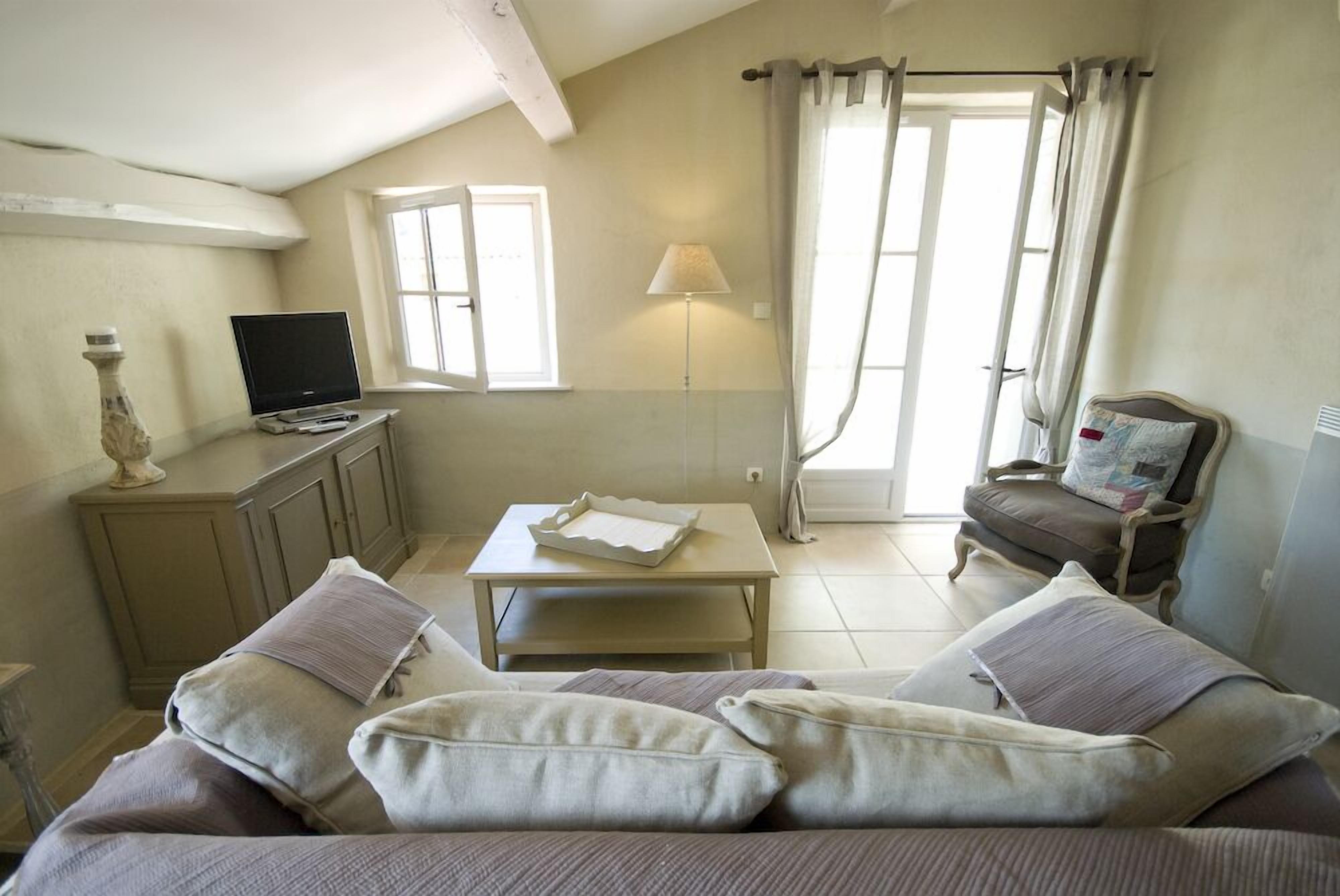 Um quarto aconchegante com sofá, mesa pequena, luminária, televisão e poltrona.
