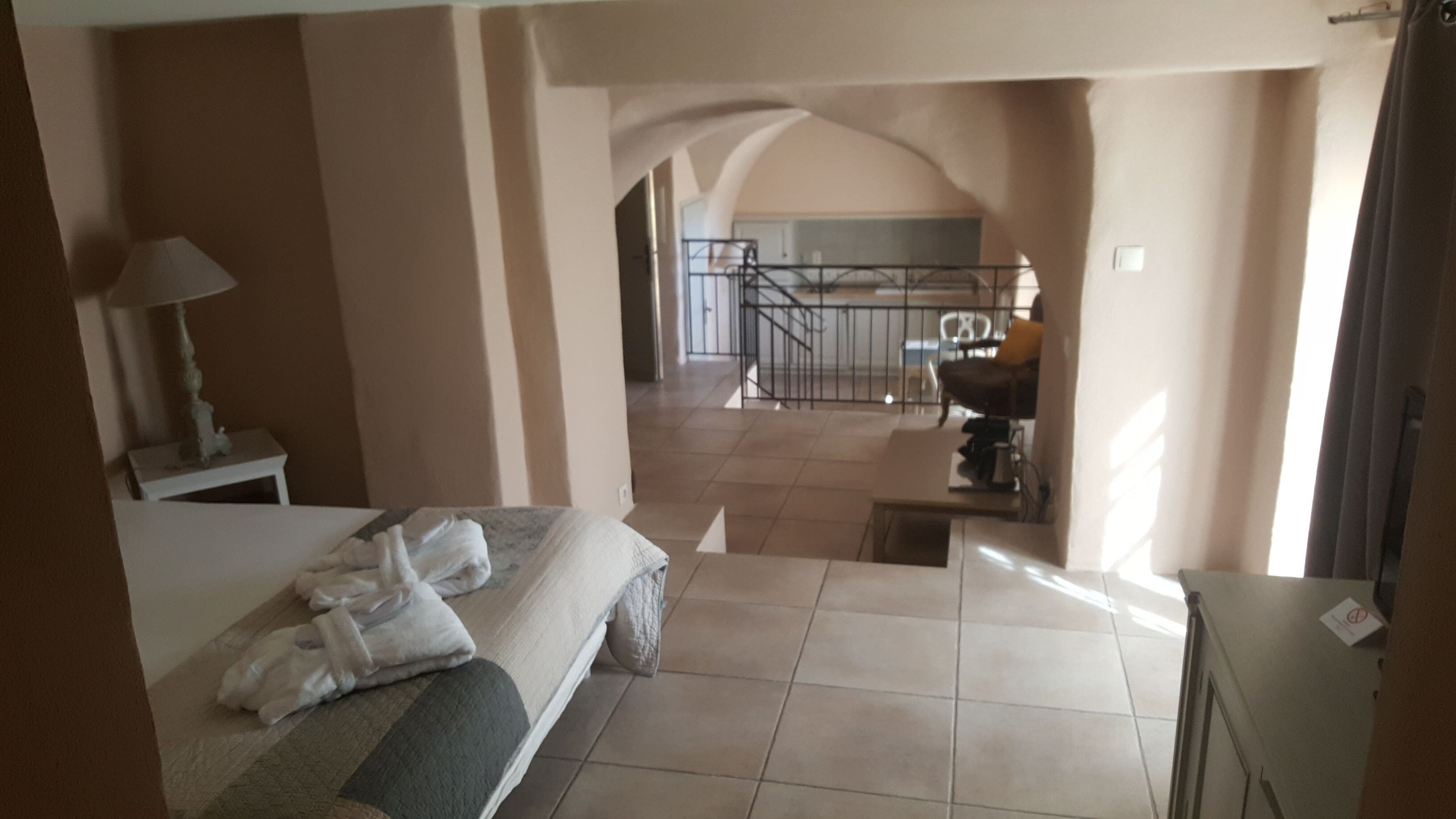 A hotel room with a bed, a nightstand, a lamp, and a view of the balcony and dining area.