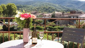 A table with a bottle and glasses, a chair, and a view of a mountainous landscape. - Couvent d'Hérépian (Herepian)