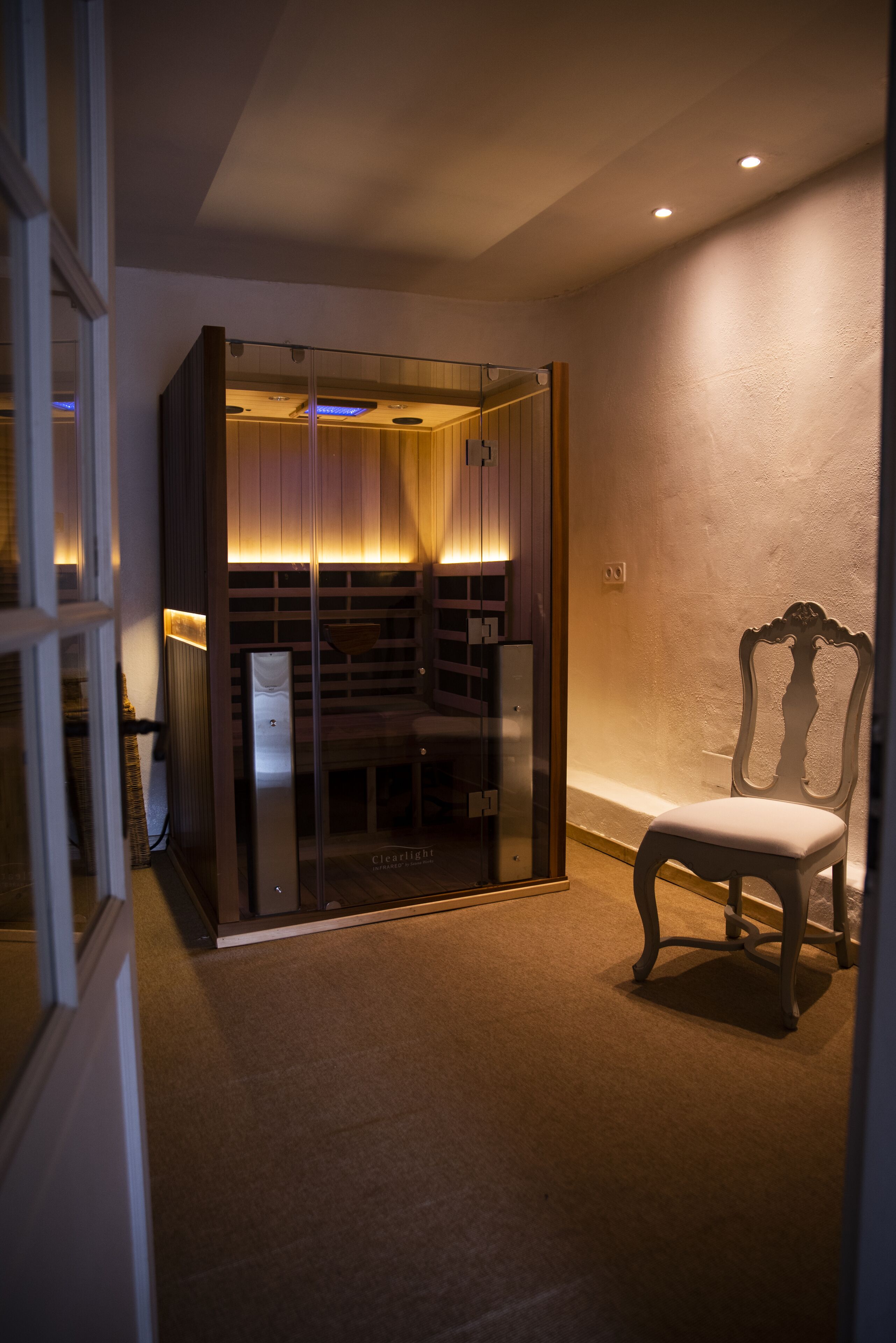 A room with a glass-enclosed sauna, a wooden chair, and a carpeted floor.