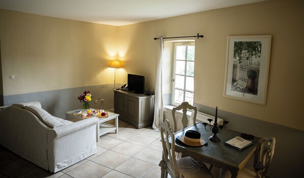 A cozy room with a sofa, a dining table with chairs, a small table with a tray of breakfast, a TV, and a window with curtains.