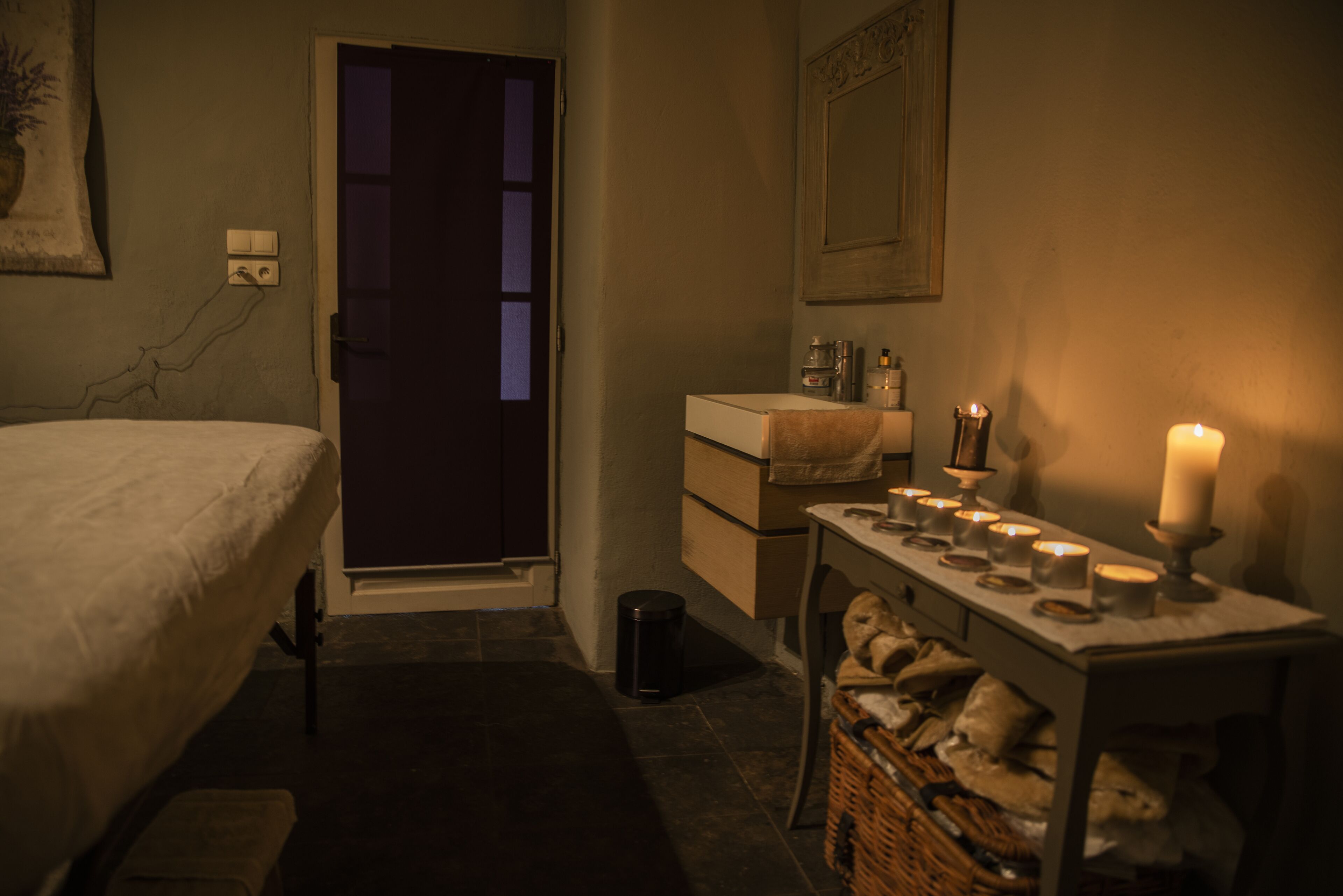 Une chambre à coucher faiblement éclairée, avec un lit, une table de chevet et une petite table sur laquelle sont posées des bougies.