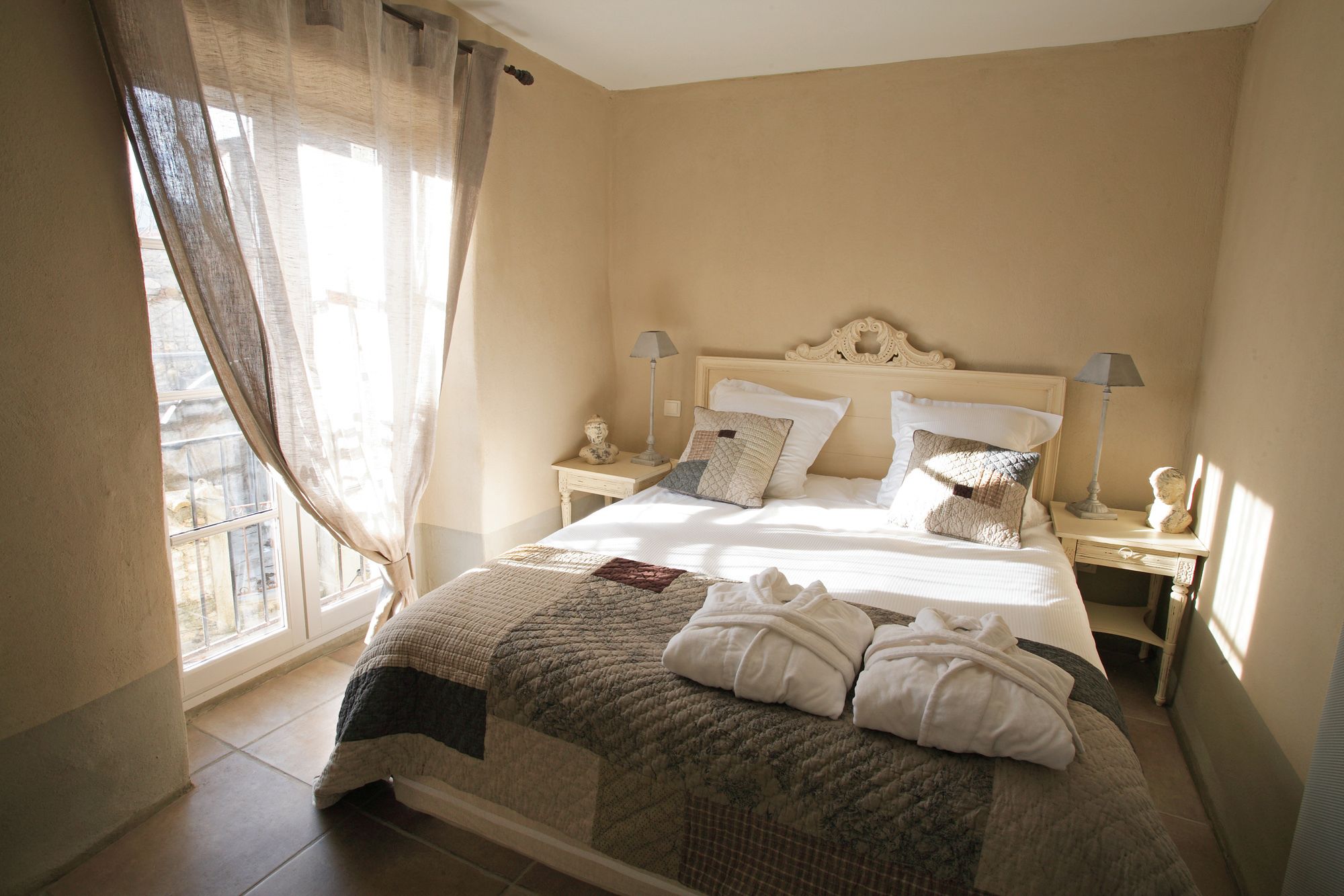 A bedroom with a large bed, two bedside tables, a window with curtains, and a view of the outside.