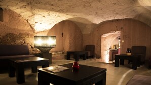 A dimly lit room with a stone wall, a sofa, a table with a lamp, and a small altar with a cross. - Couvent d'Hérépian (Herepian)
