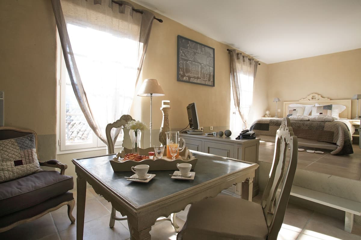 A hotel room with a dining area, a bed, and a painting on the wall.