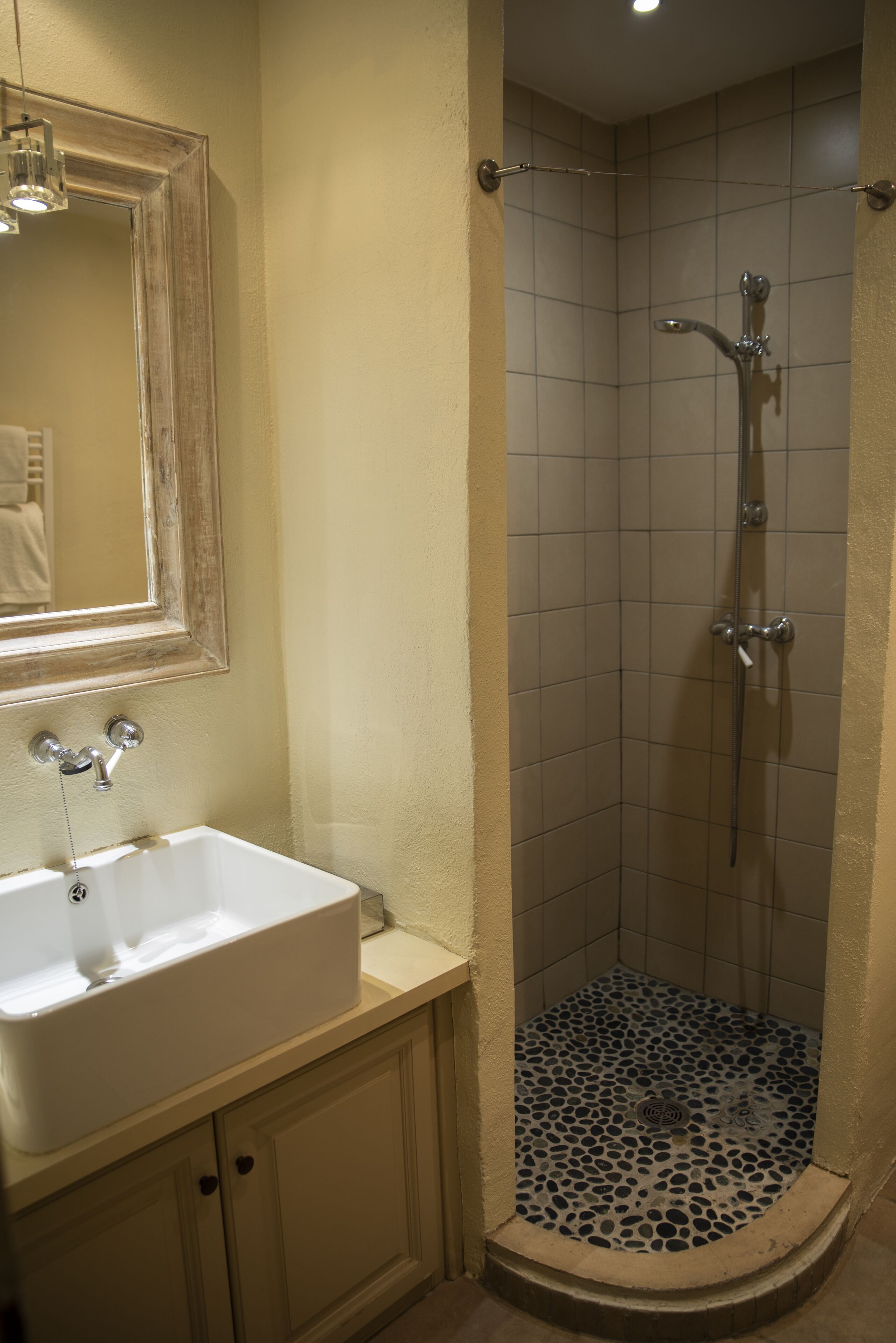 A bathroom with a white sink, a mirror, and a shower with a tiled floor.