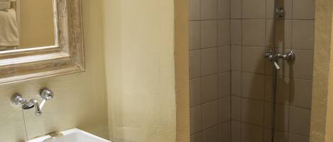A bathroom with a white sink, a mirror, and a shower with a tiled floor.