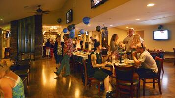 A restaurant with wooden flooring, tables, chairs, and a television mounted on the wall.