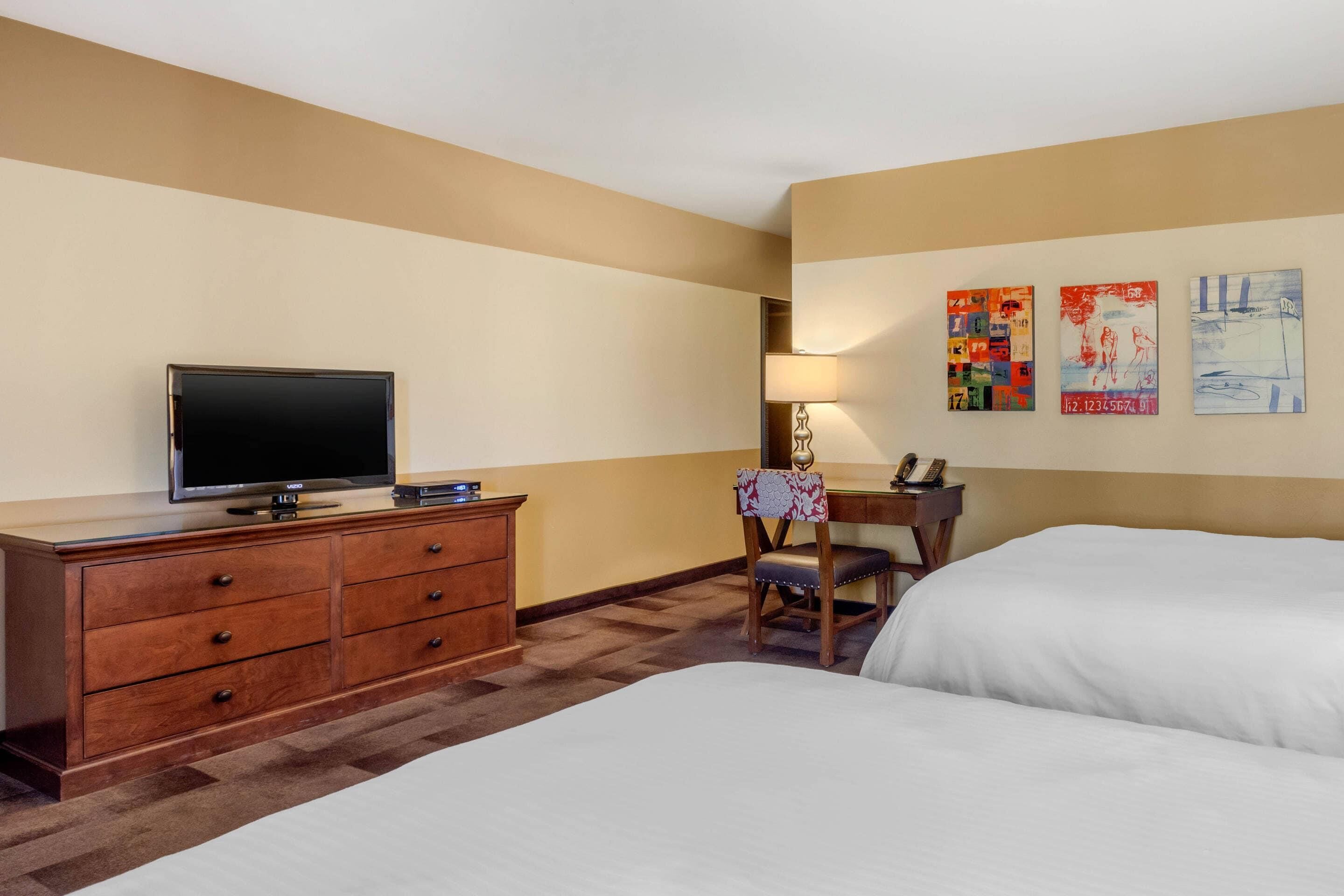 Een hotelkamer met twee bedden, een televisie, een bureau met stoel, en kunst aan de muur.
