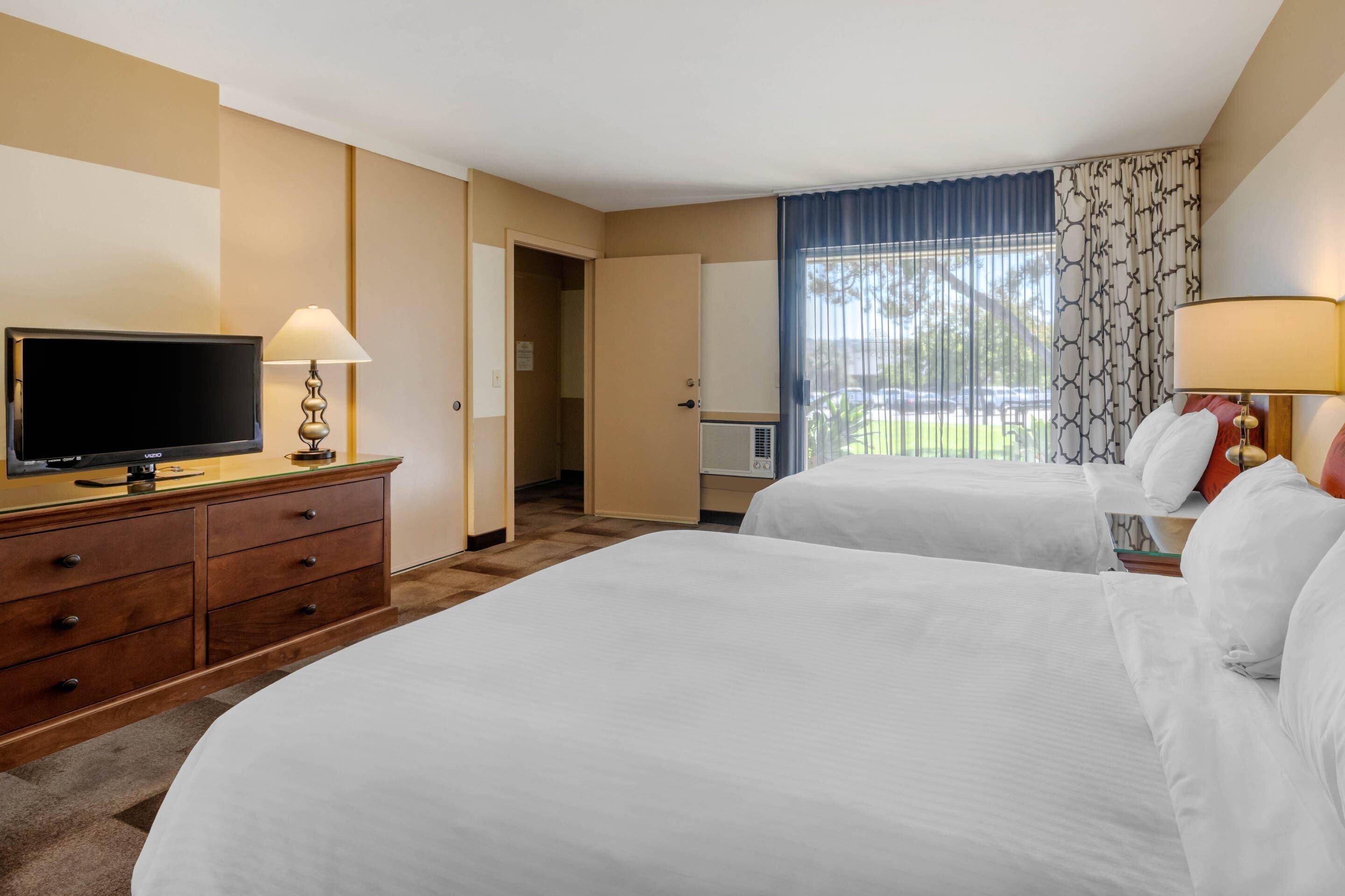 Una habitación de hotel con dos camas, televisión, cómoda y ventana con cortinas.