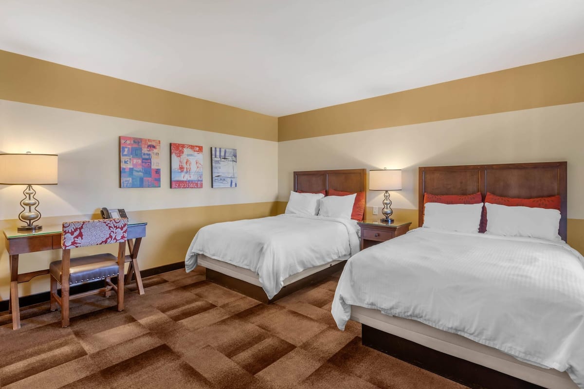 A hotel room with two beds, a desk, and a chair.