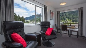 Ein Zimmer mit zwei Ledersesseln, einem kleinen Tisch und Blick auf eine gebirgige Landschaft durch große Fenster.