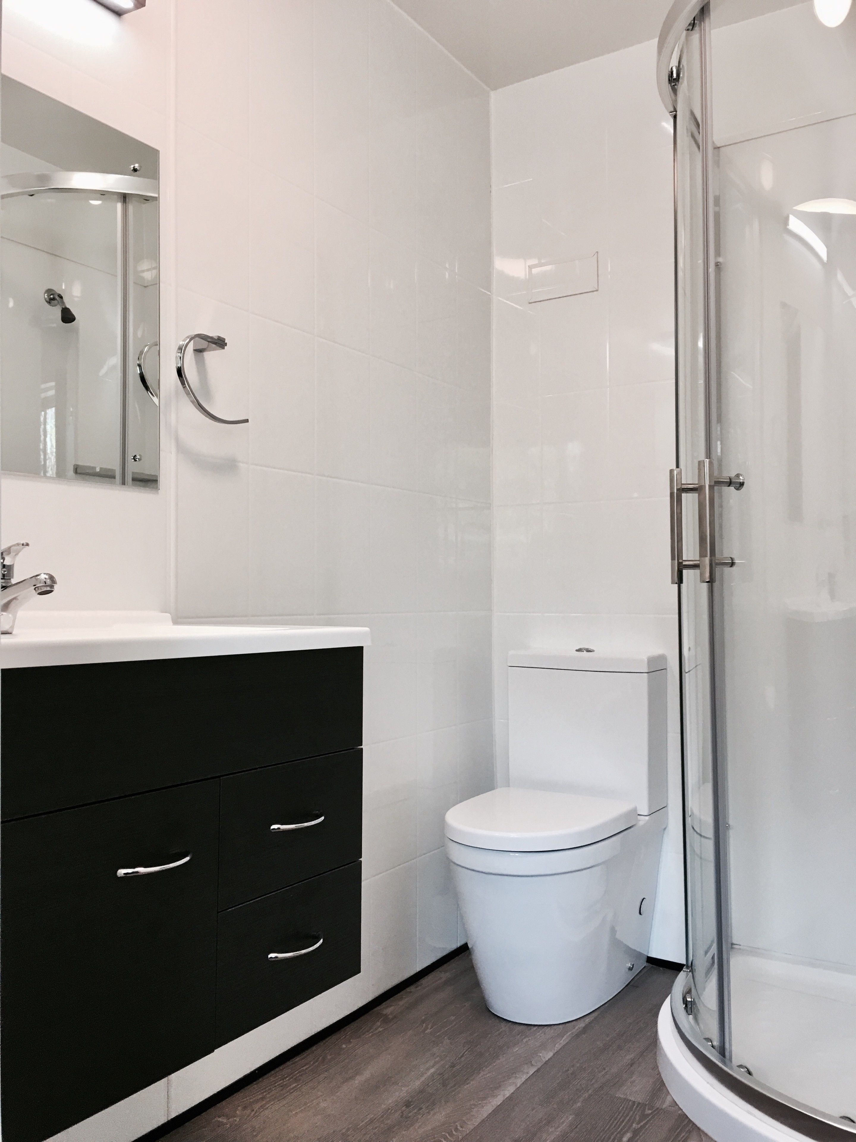 Un bagno moderno con cabina doccia in vetro, un water bianco e un mobile lavabo nero con cassetti.