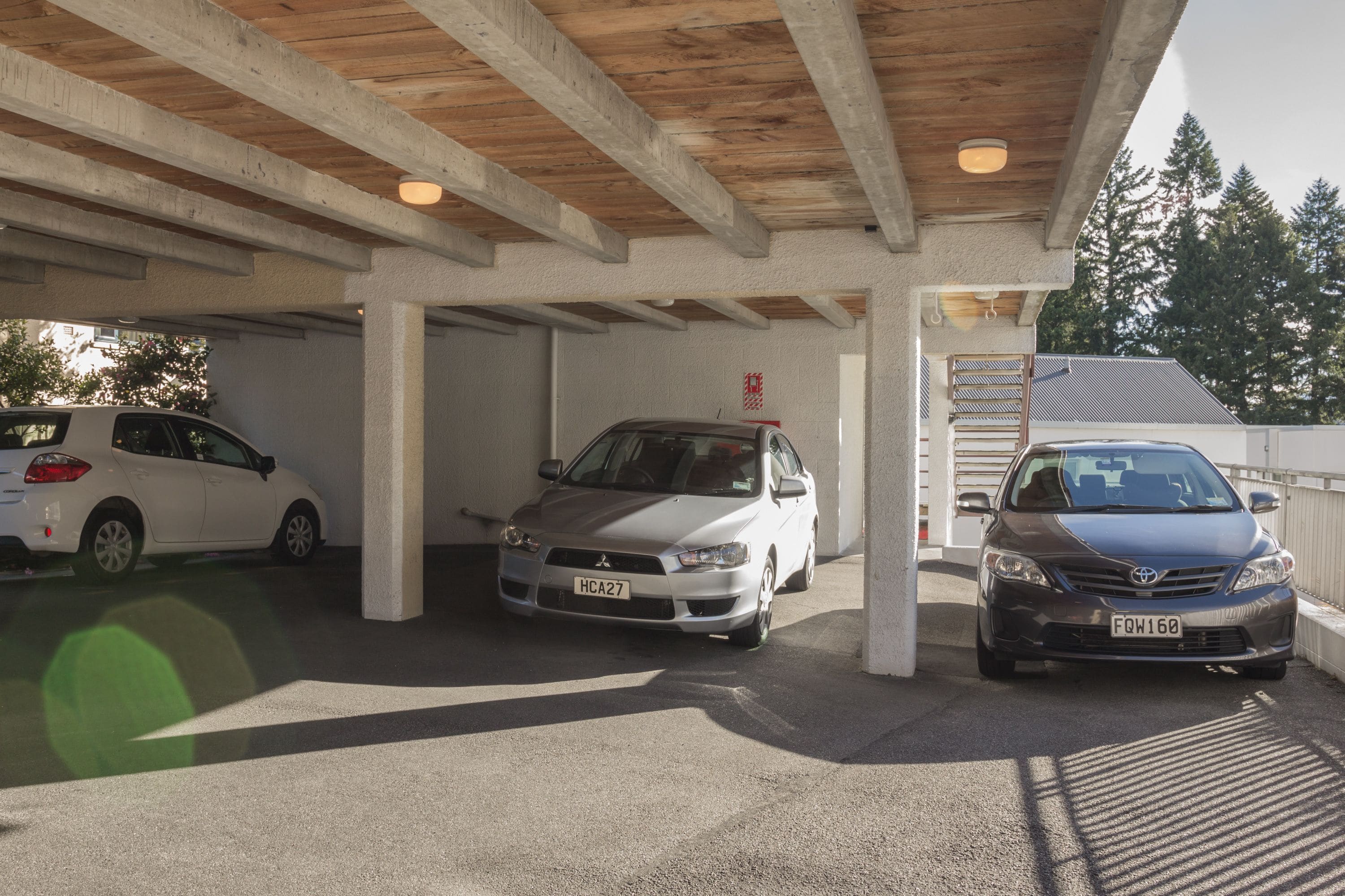 A covered parking area with three cars parked under a wooden beam structure.