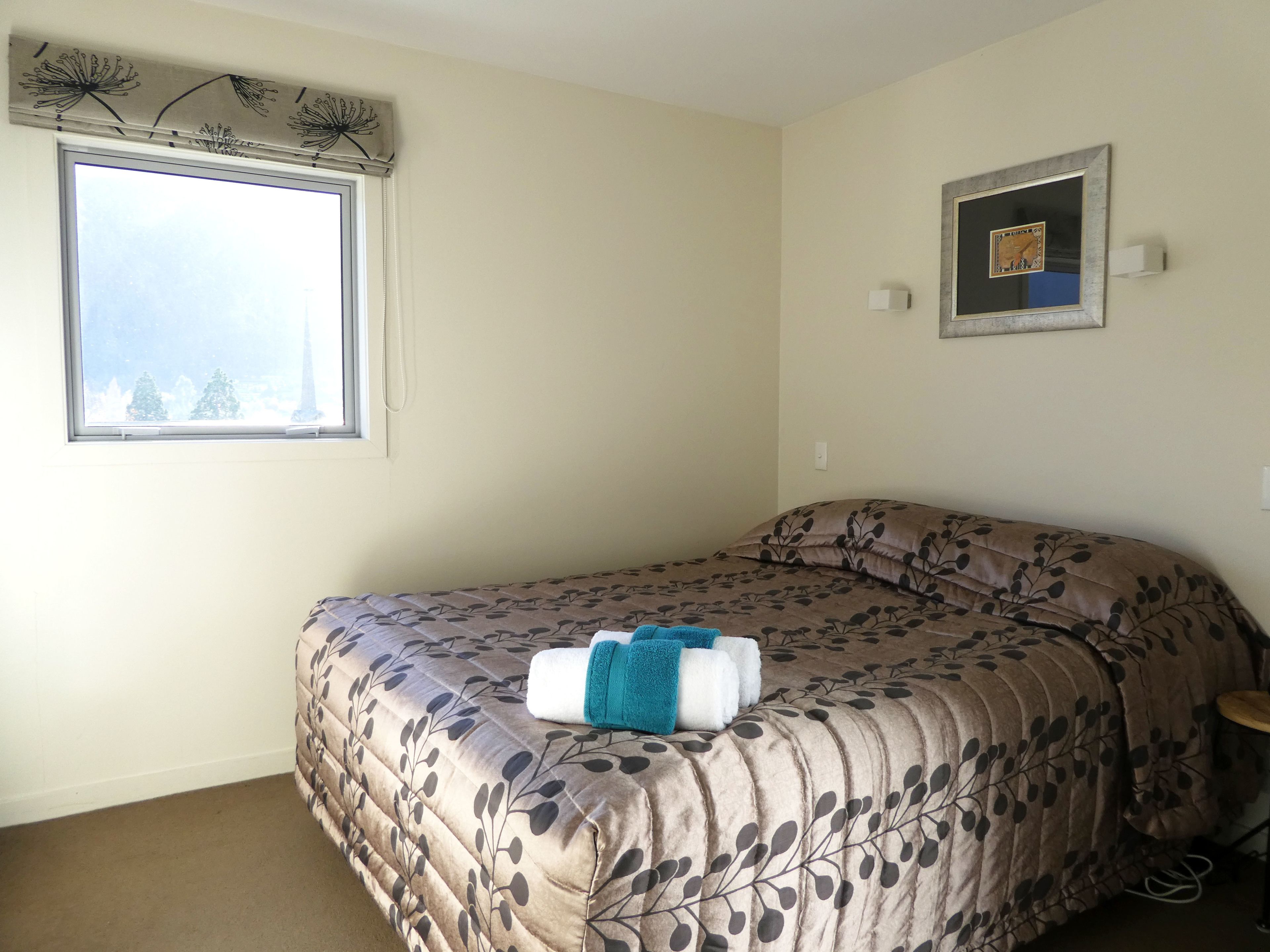 Een slaapkamer met een bed, een raam, een wandklok en een lijst met een afbeelding.