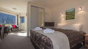 A hotel room with a bed, a desk, and a chair. There is a painting on the wall and a window with a view.