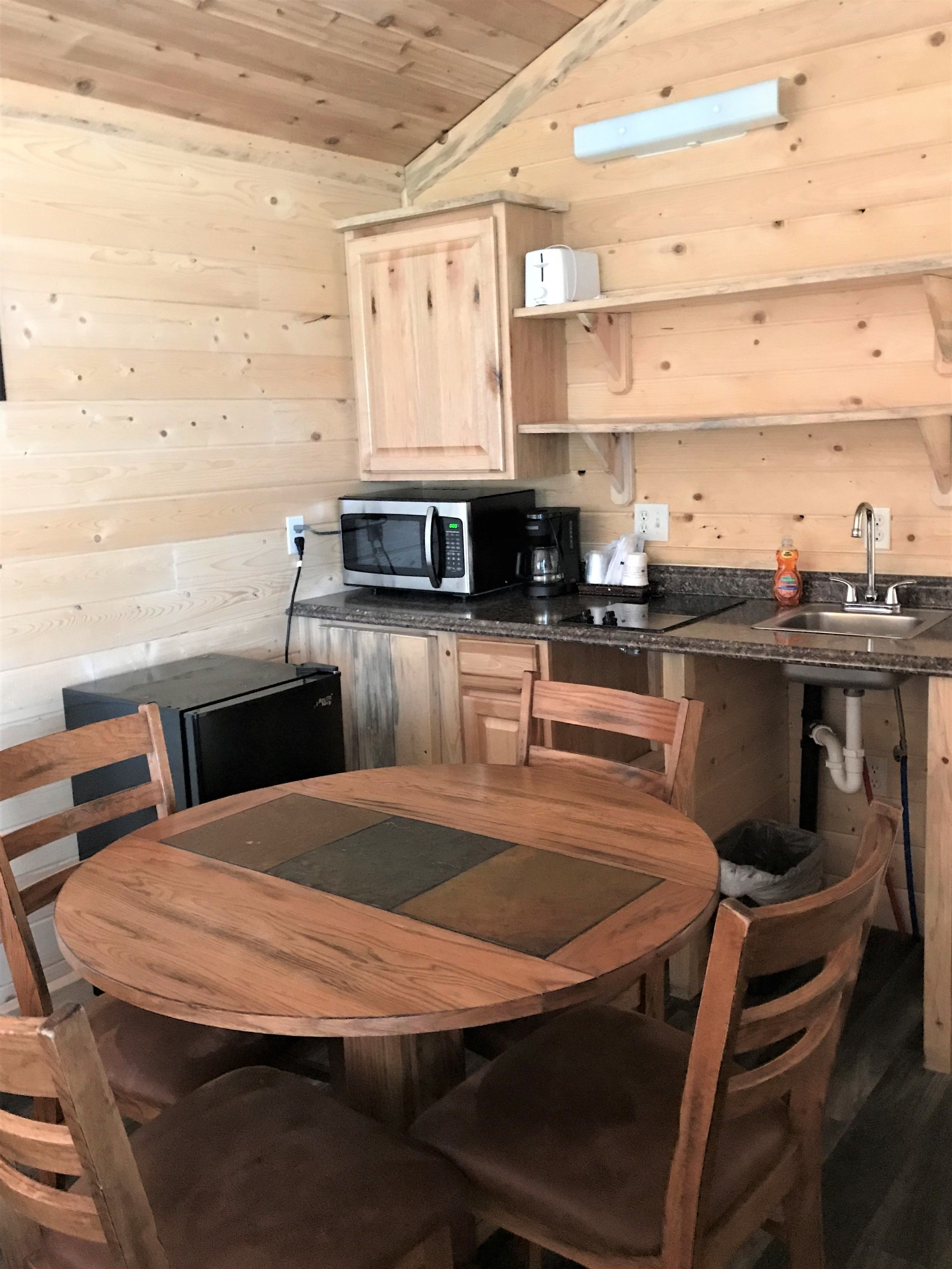 A compact kitchen with a microwave, coffee maker, and sink. There is a round wooden table with chairs.