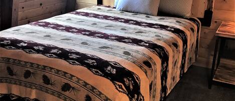 Un dormitorio de cabaña de madera con una cama, dos almohadas, una mesita de noche y una ventana.