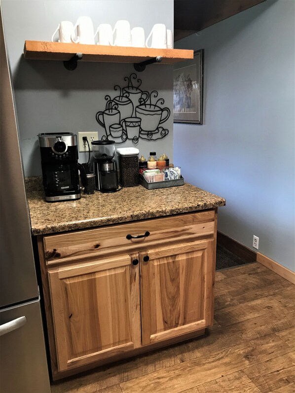 A kitchen with a coffee maker, a coffee pot, and a coffee grinder on the counter. There is a wooden cabinet below the counter. - Drift Lodge & Fly Shop (Island Park)