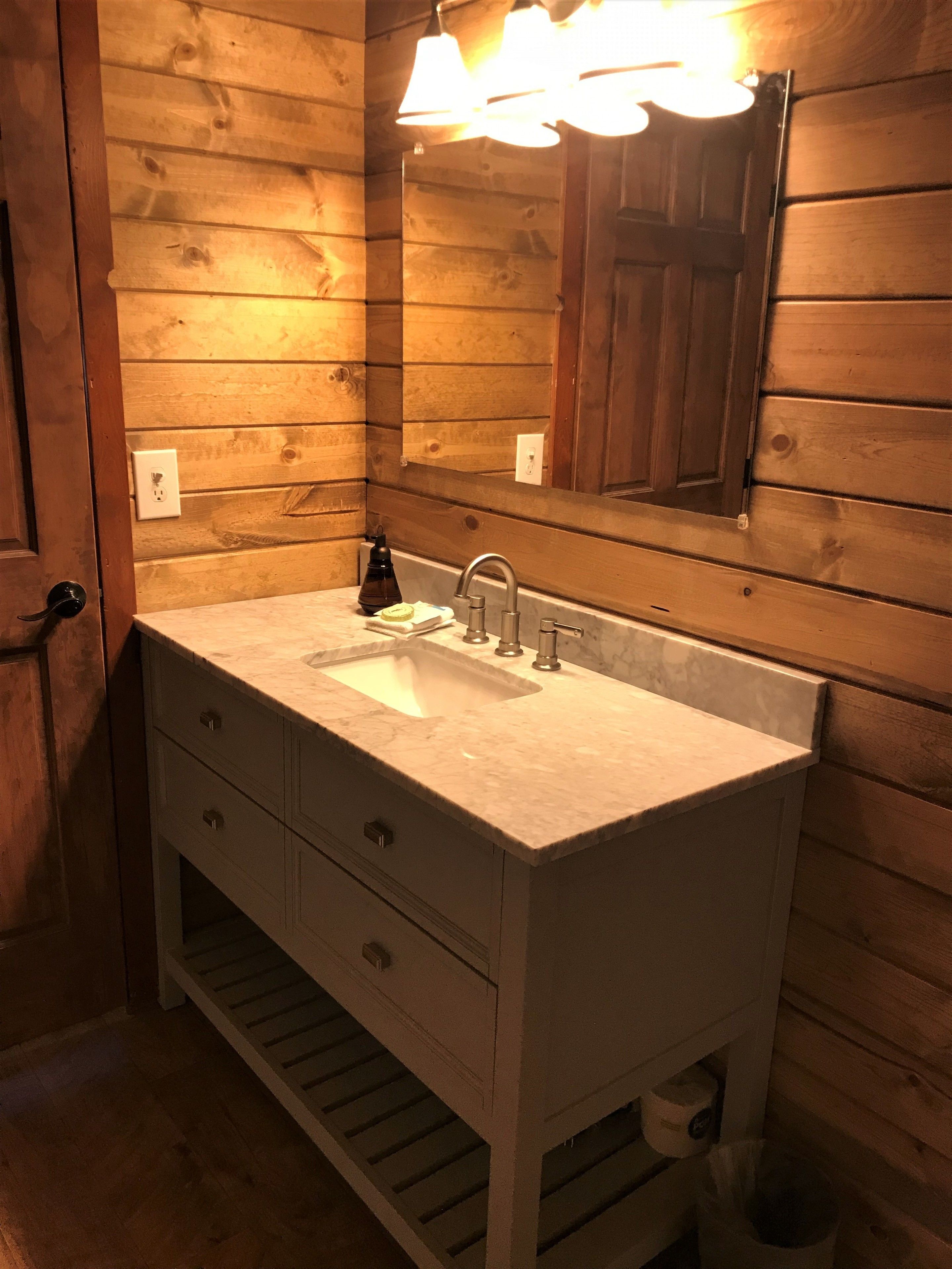 Ein Badezimmer mit Holzwand, einem weißen Waschbecken und einem Spiegel darüber sowie einer Leuchte über dem Spiegel.