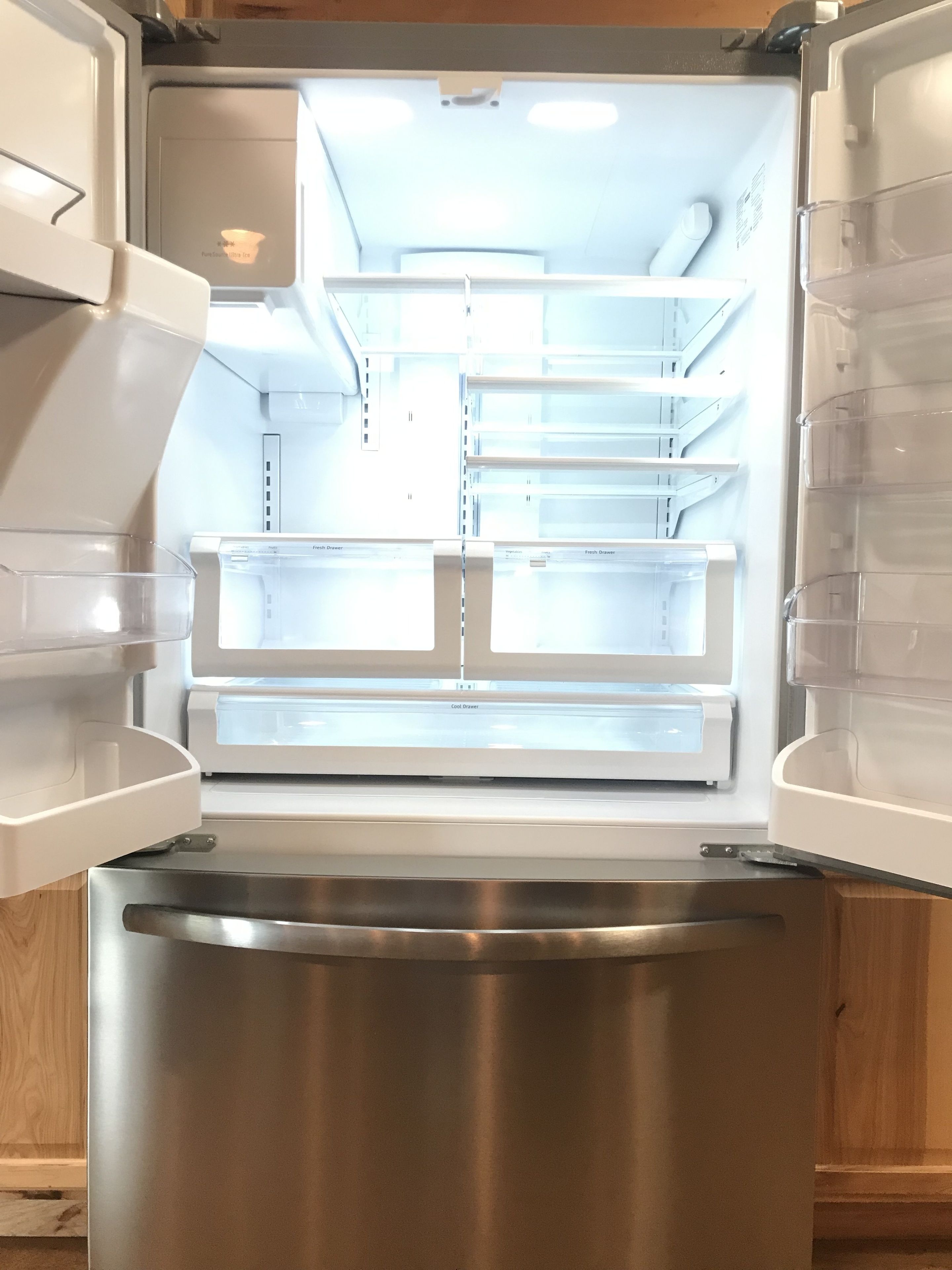 An open refrigerator with multiple shelves and drawers, a stainless steel freezer, and a wooden cabinet door.