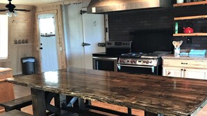 Uma cozinha com uma grande mesa de madeira, dois fornos e um revestimento de tijolos.